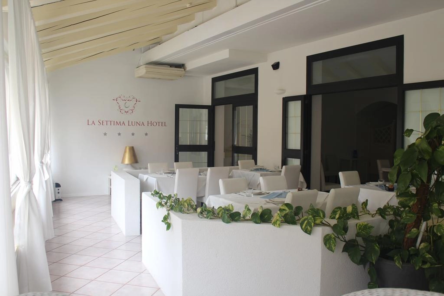 Izudin Jasarevic – Pflege mit Menschlichkeit – Innenansicht eines hellen, minimalistischen Speisesaals im La Settima Luna Hotel, einem Boutique-Hotel in Lipari, Italien. Der Raum ist überwiegend in Weiß gehalten: weiß getünchte Wände, weiß gedeckte Tische und moderne weiße Stühle spiegeln das „weiße Thema“ und die minimalistische Einrichtung des Hotels wider.